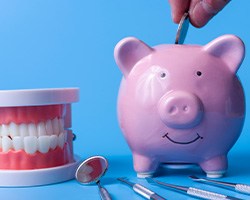 A piggy bank next to dental instruments along a blue background