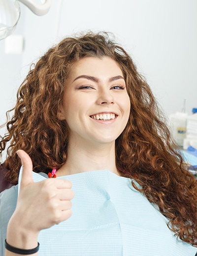 a smiling dental patient giving a thumbs up 