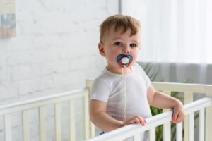 Child standing in crib, sucking on pacifier